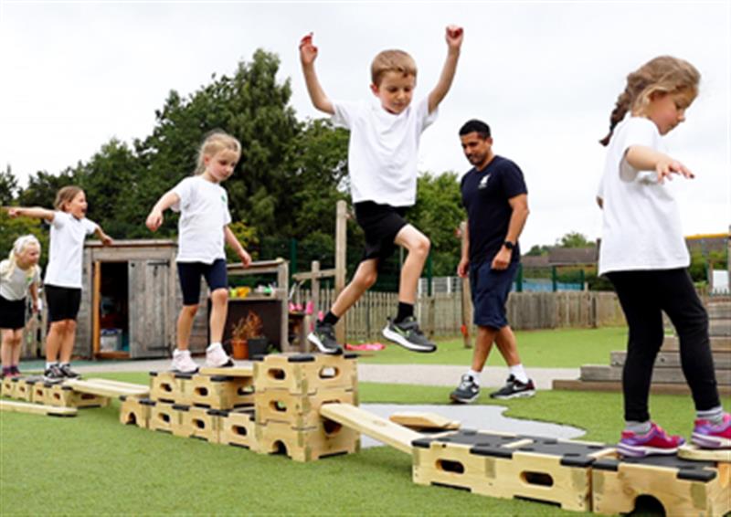 Five children taking it in turns to balance and leap across a Play Builder trail without falling off.